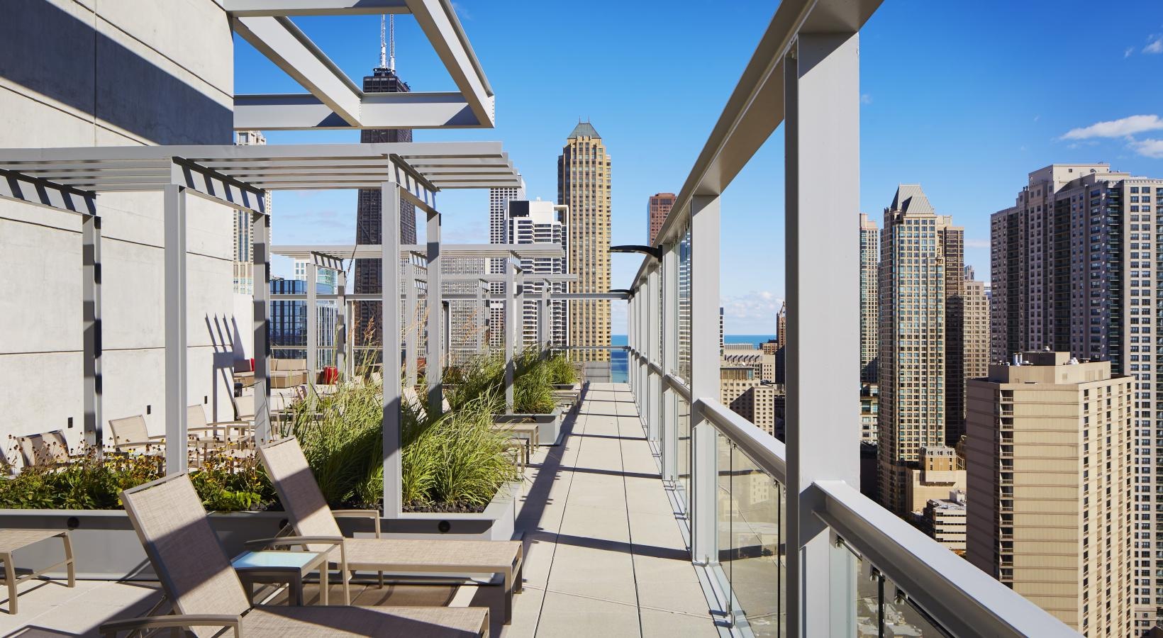 Spacious balconies a walkway with chairs and tables on it and buildings in the background