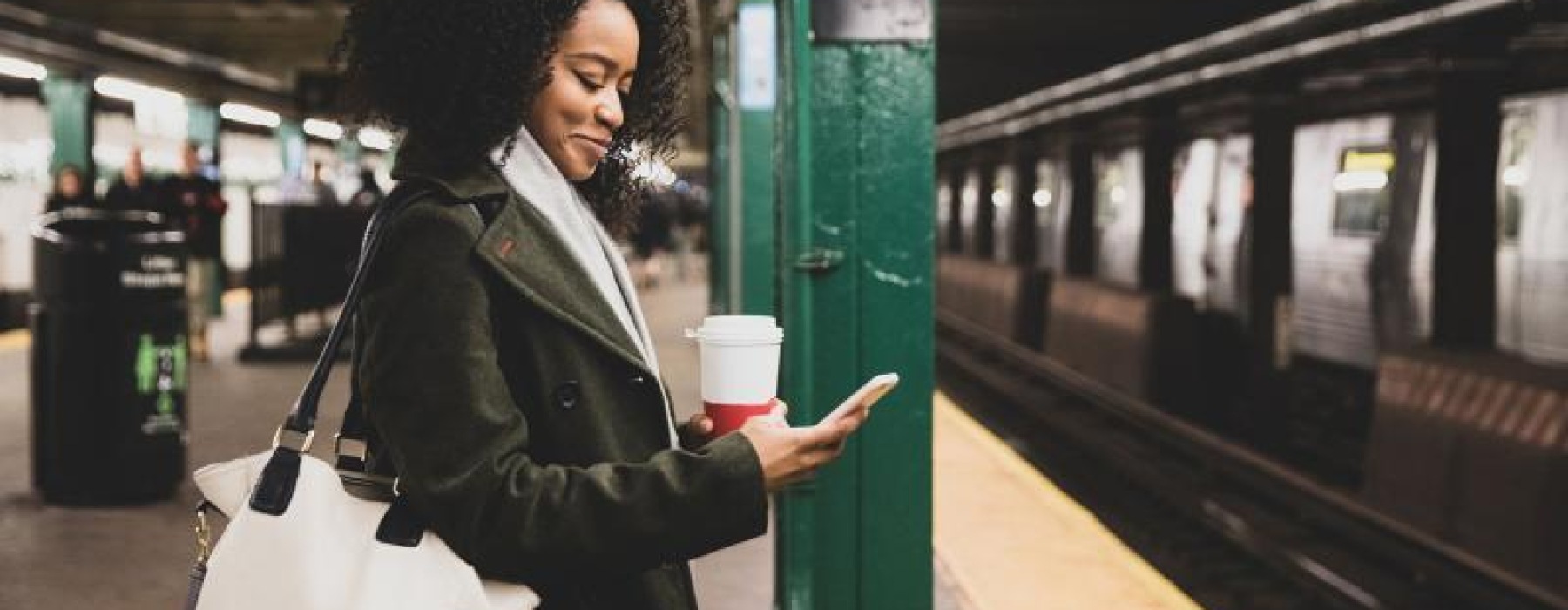 woman with a cup of coffee texts on subway station platform